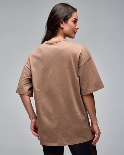 Taupe oversized short-sleeve T-shirt with a plain back and crew neckline, shown from the back on a female model wearing black leggings against a light gray studio background.