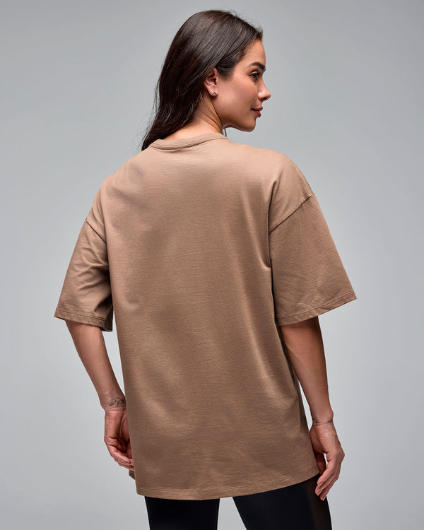 Taupe oversized short-sleeve T-shirt with a plain back and crew neckline, shown from the back on a female model wearing black leggings against a light gray studio background.