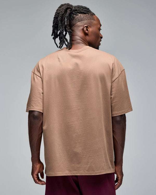 Taupe oversized short-sleeve T-shirt with a plain back and crew neckline, shown from the back on a male model wearing burgundy athletic shorts against a light gray studio background.