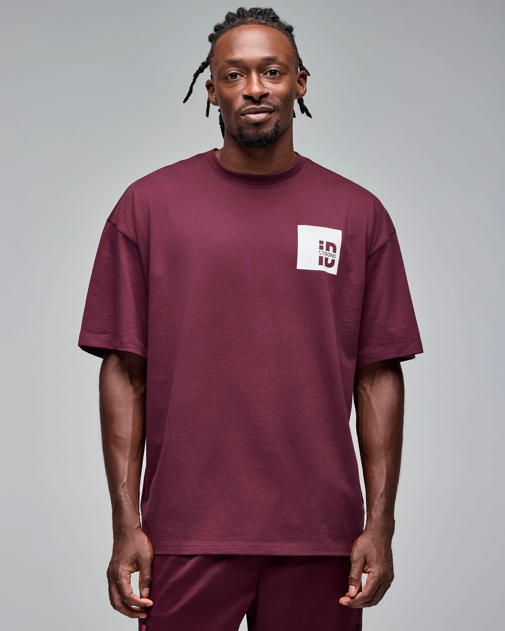 Burgundy oversized short-sleeve T-shirt with a small white chest logo patch. Male model wears the relaxed tee with burgundy shorts against a light gray background.