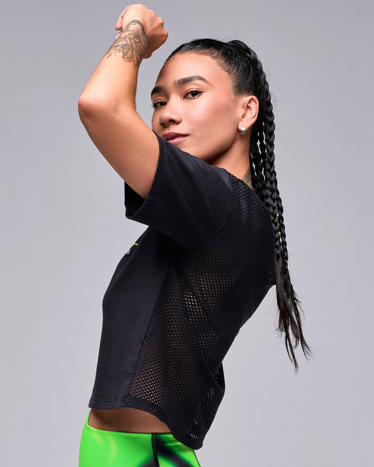 Female model with one arm raised in the black 'STRONG' boxy top, shown in side view with the mesh back and short sleeves.