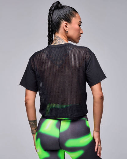 Shown from the back, the black 'STRONG' boxy top's sheer mesh back panel, with neon green and black swirl print leggings.