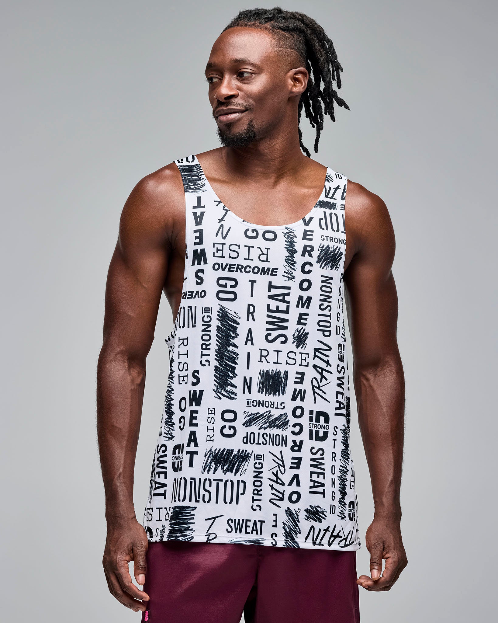 White graphic-print athletic tank with a scoop neckline and deep-cut armholes, shown full length on a male model wearing burgundy athletic shorts against a light gray studio background.