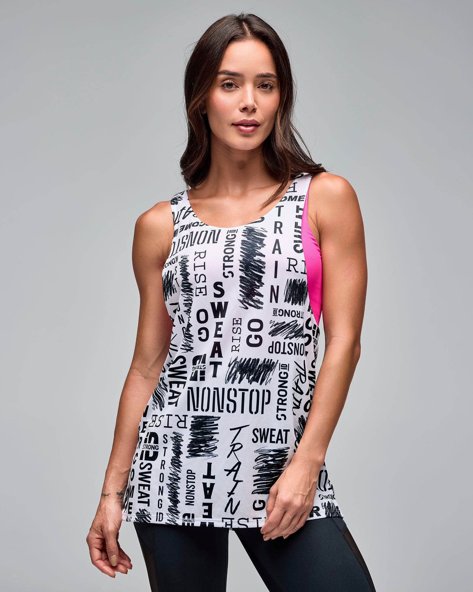 White graphic-print athletic tank with a scoop neckline and longline fit, shown on a female model layered over a pink sports bra and paired with black leggings against a light gray studio background.
