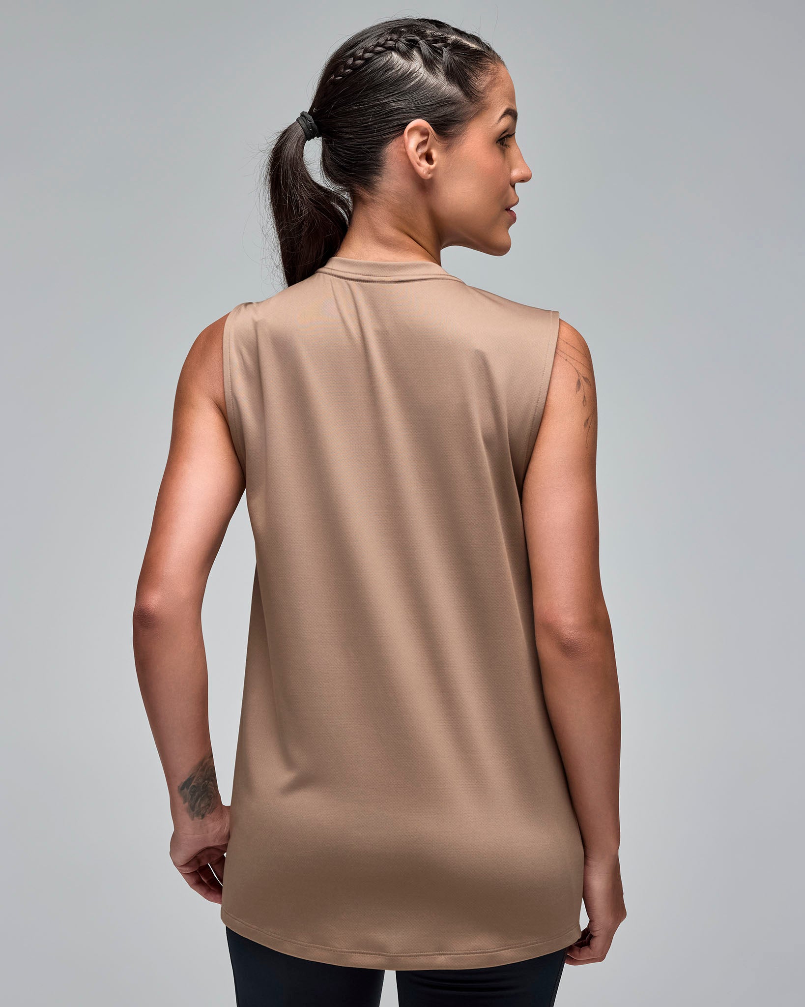 Taupe sleeveless athletic tank with a crew neckline and clean back, shown from the back on a female model wearing black leggings against a light gray studio background.