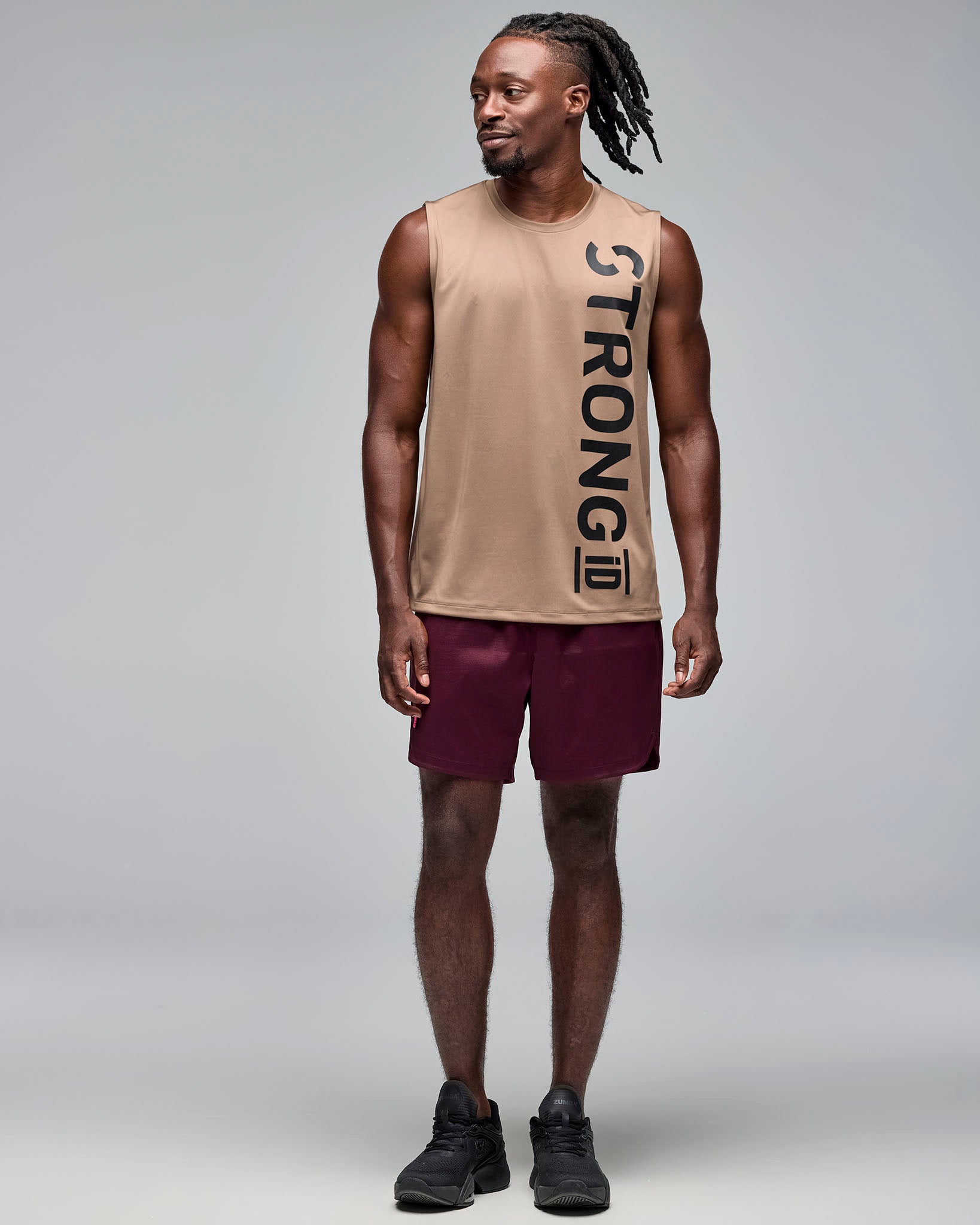 Taupe sleeveless athletic tank with a crew neckline and oversized vertical black "STRONG iD" logo, shown full length on a male model wearing burgundy athletic shorts and black sneakers.