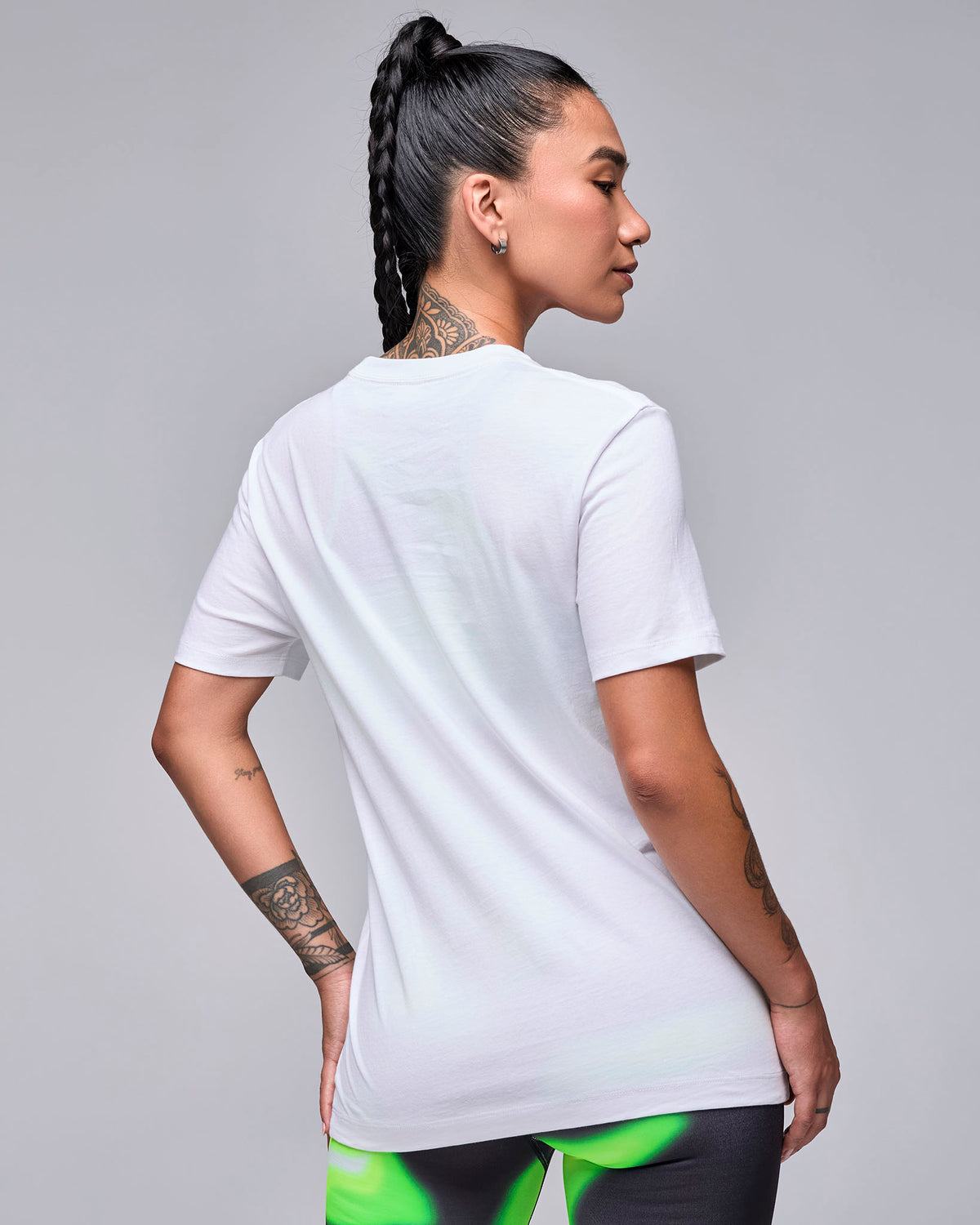 Back view of a female model in the white 'STRONG iD' graphic tee, showing a plain back and relaxed fit, with swirl print leggings.