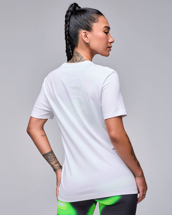 Back view of a female model in the white 'STRONG iD' graphic tee, showing a plain back and relaxed fit, with swirl print leggings.