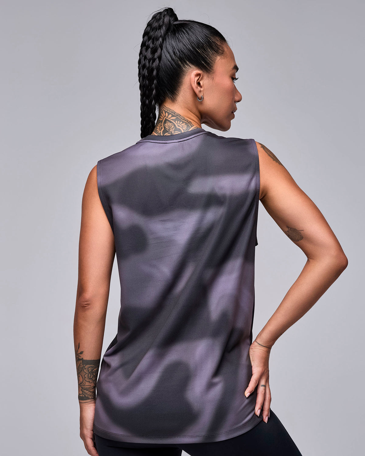 Shown from the back, a female model in the black and grey swirl print tank, with a long, loose fit and plain back.