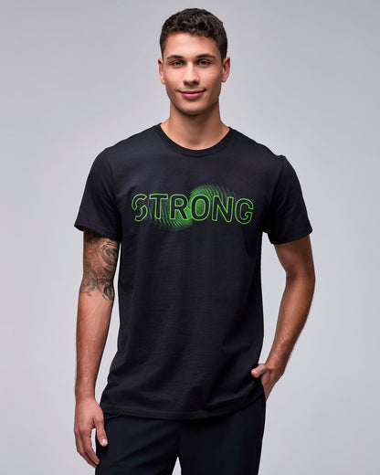 Male model in the black 'STRONG' wave-like graphic tee, one hand in the pocket of his black pants.