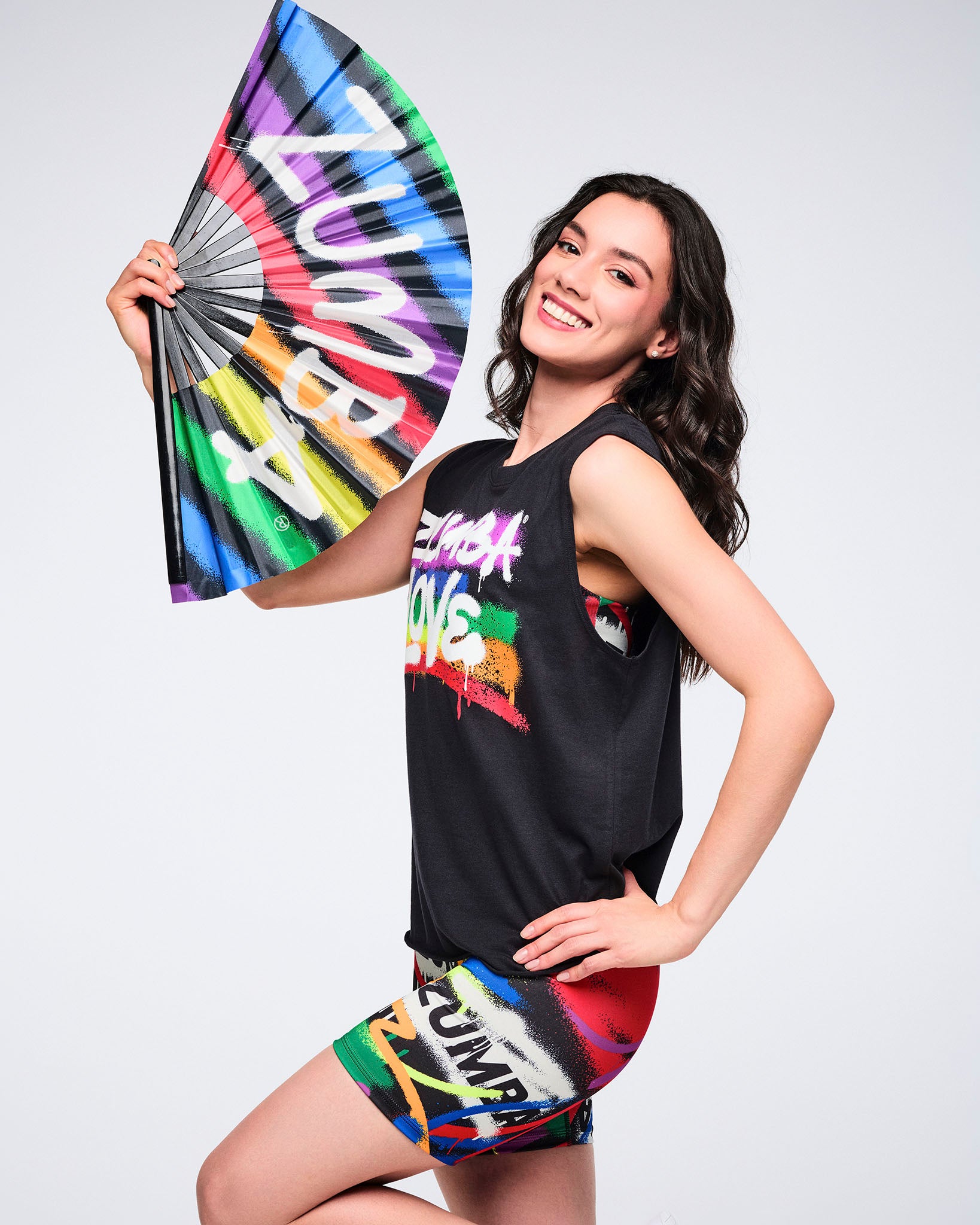 Female model in colorful Zumba Wear holding a colorful fan with black trim on a white background.