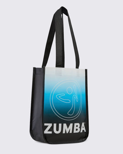 Angled view of the reusable tote, showing the black side gusset next to the white-to-blue-to-black gradient front with the Zumbito and 'ZUMBA' text.