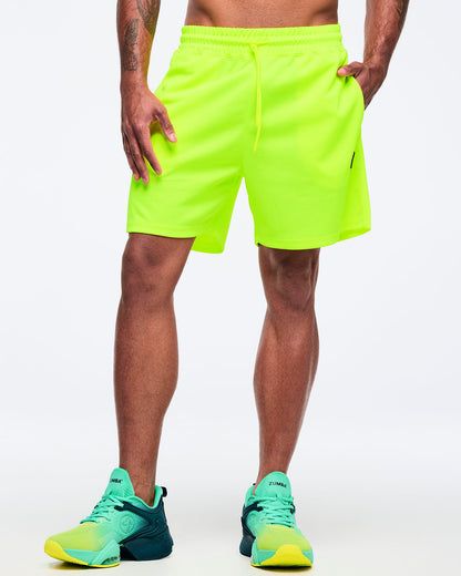 Neon lime athletic shorts with elastic drawstring waistband and relaxed fit, shown from the front on a male model wearing teal-to-lime athletic sneakers on a white studio background.