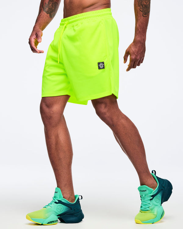 Neon lime athletic shorts with elastic waistband and loose, mid-thigh length fit, shown in side view on a male model wearing teal-to-lime athletic sneakers on a white studio background.