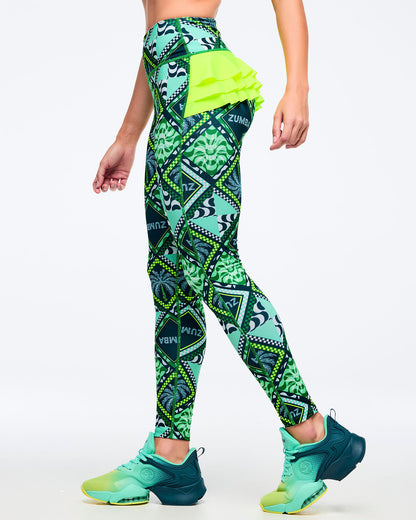 Green geometric-print high-waisted leggings with neon lime triple-tier ruffle at the back, shown in side view on a female model wearing teal-to-lime athletic sneakers on a white studio background.