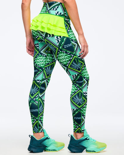 Green geometric-print high-waisted leggings with neon lime layered ruffle detail across the back waistband, shown from the back on a female model wearing teal-to-lime athletic sneakers on a white studio background.