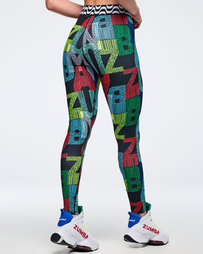 Back view of the multicolor letter-print leggings with black-and-white wavy waistband; female model wears white high-top Zumba sneakers on a white background.