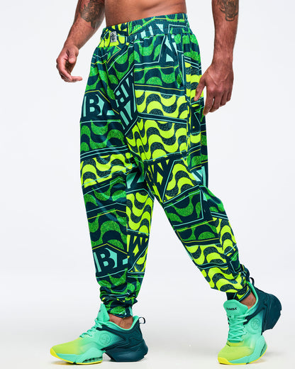 View of a male model wearing neon green/teal graphic Zumba jogger pants; teal-and-lime Zumba sneakers on a white background.