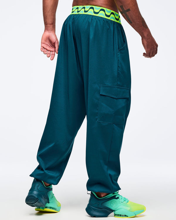 Teal cargo jogger pants with a neon green-and-black wave print waistband, shown from the back on a male model; loose fit with cargo pocket detail, elastic cuffs, and aqua-to-lime sneakers.