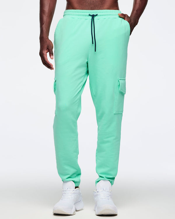 Mint green cargo jogger pants shown from the front on a male model; elastic drawstring waistband, thigh cargo pockets, and tapered ankles, paired with white sneakers.