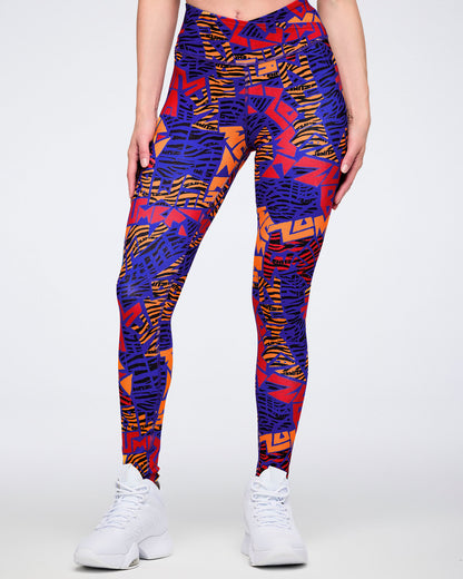 Front view of blue, orange, and red abstract-print high-waisted leggings with a wide crossover-style waistband and fitted full-length silhouette. Female model wears the leggings with white athletic sneakers.