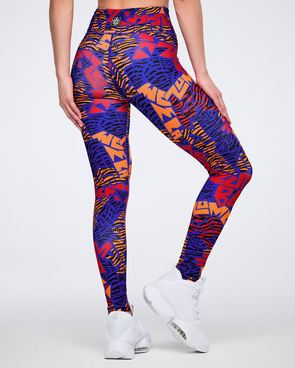 Back view of blue, orange, and red abstract-print high-waisted leggings with a wide waistband, fitted silhouette, and full-length leg. Female model wears the leggings with white athletic sneakers.