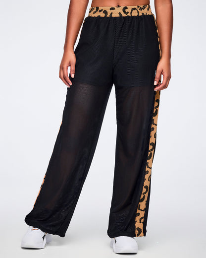Black mesh wide-leg pants with a sheer finish, tan leopard-print waistband, and matching leopard-print side stripes, shown from the front on a female model wearing white sneakers.