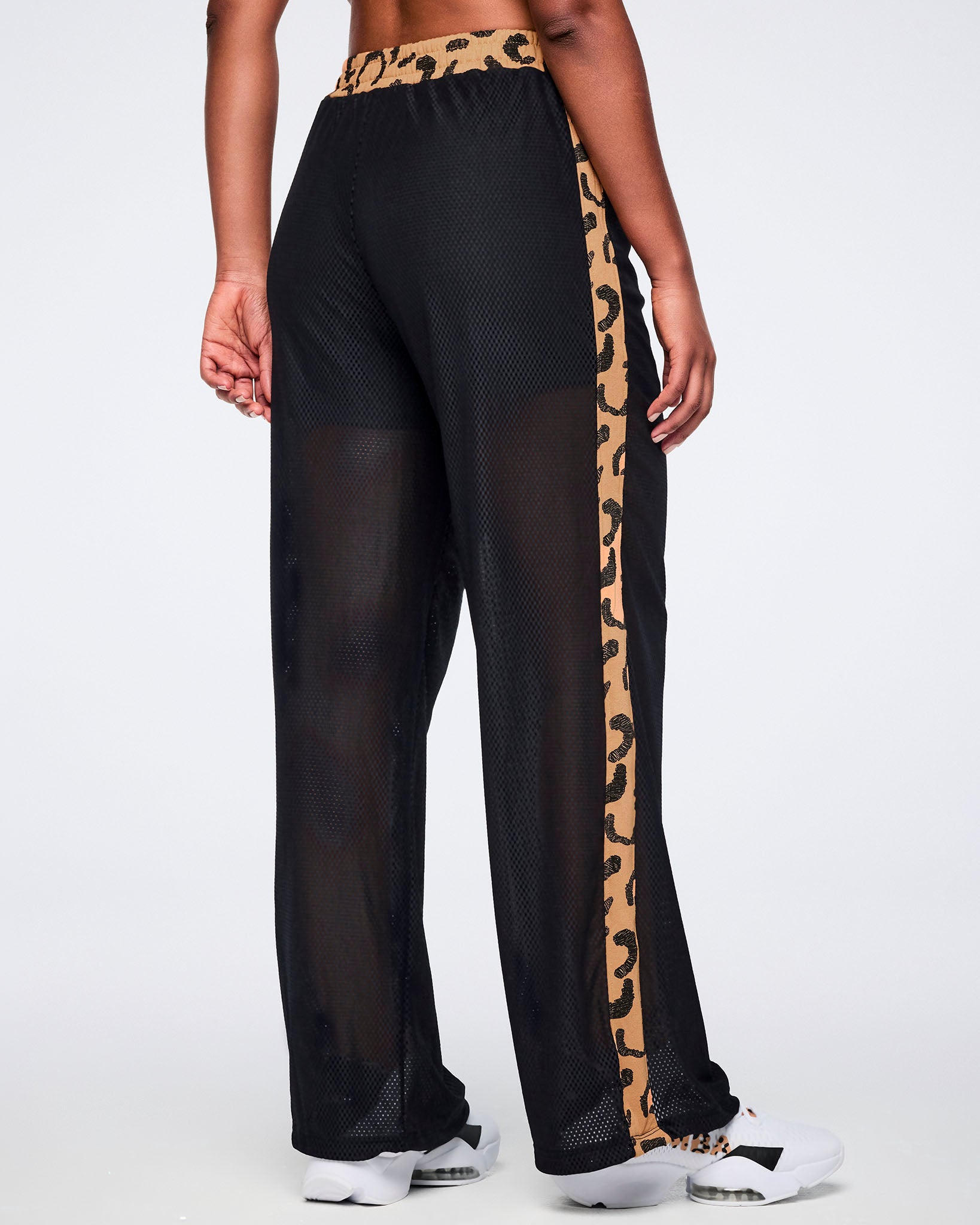 Black mesh wide-leg pants with a sheer finish, tan leopard-print waistband, and matching leopard-print side stripes, shown from the back on a female model wearing white sneakers.