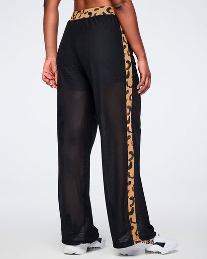 Black mesh wide-leg pants with a sheer finish, tan leopard-print waistband, and matching leopard-print side stripes, shown from the back on a female model wearing white sneakers.