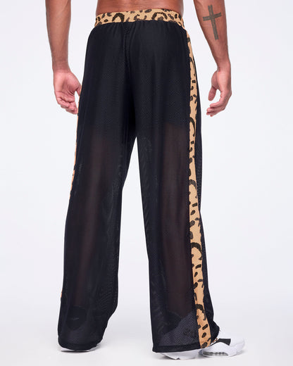 Black mesh wide-leg pants with a sheer finish, tan leopard-print waistband, and matching leopard-print side stripes, shown from the back on a male model wearing white sneakers.