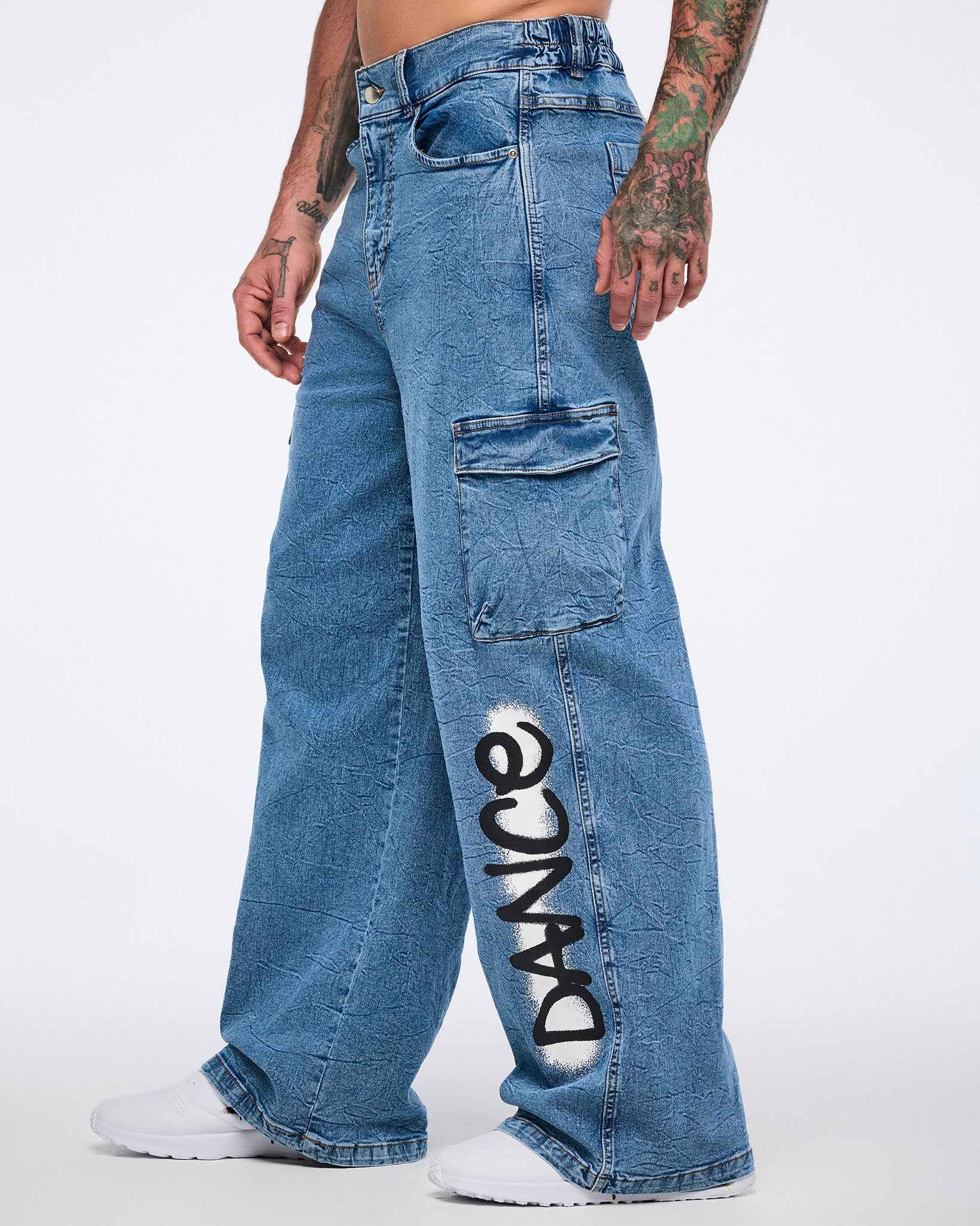 Male model side view in denim cargo pants with “DANCE” on the left leg and cargo pocket against a white background.