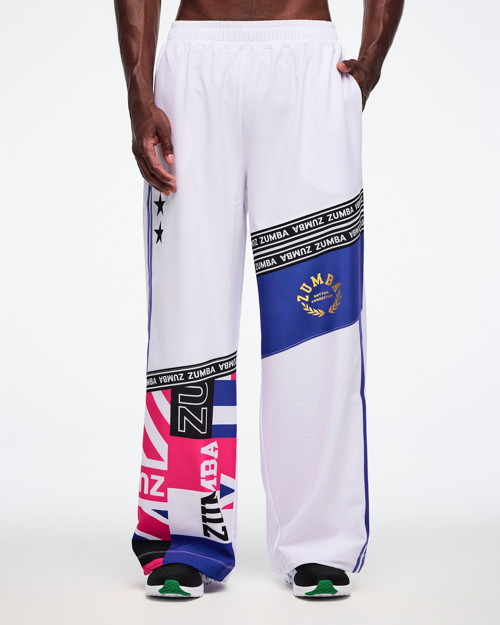Male model with left hand in pocket, wearing white pants with colorful Zumba branding on a white background.