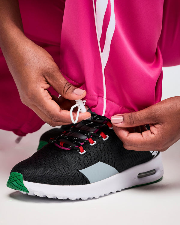 Close-up of bright pink pants with adjustable cuffs in use, paired with a black Zumba athletic shoe on a white background.