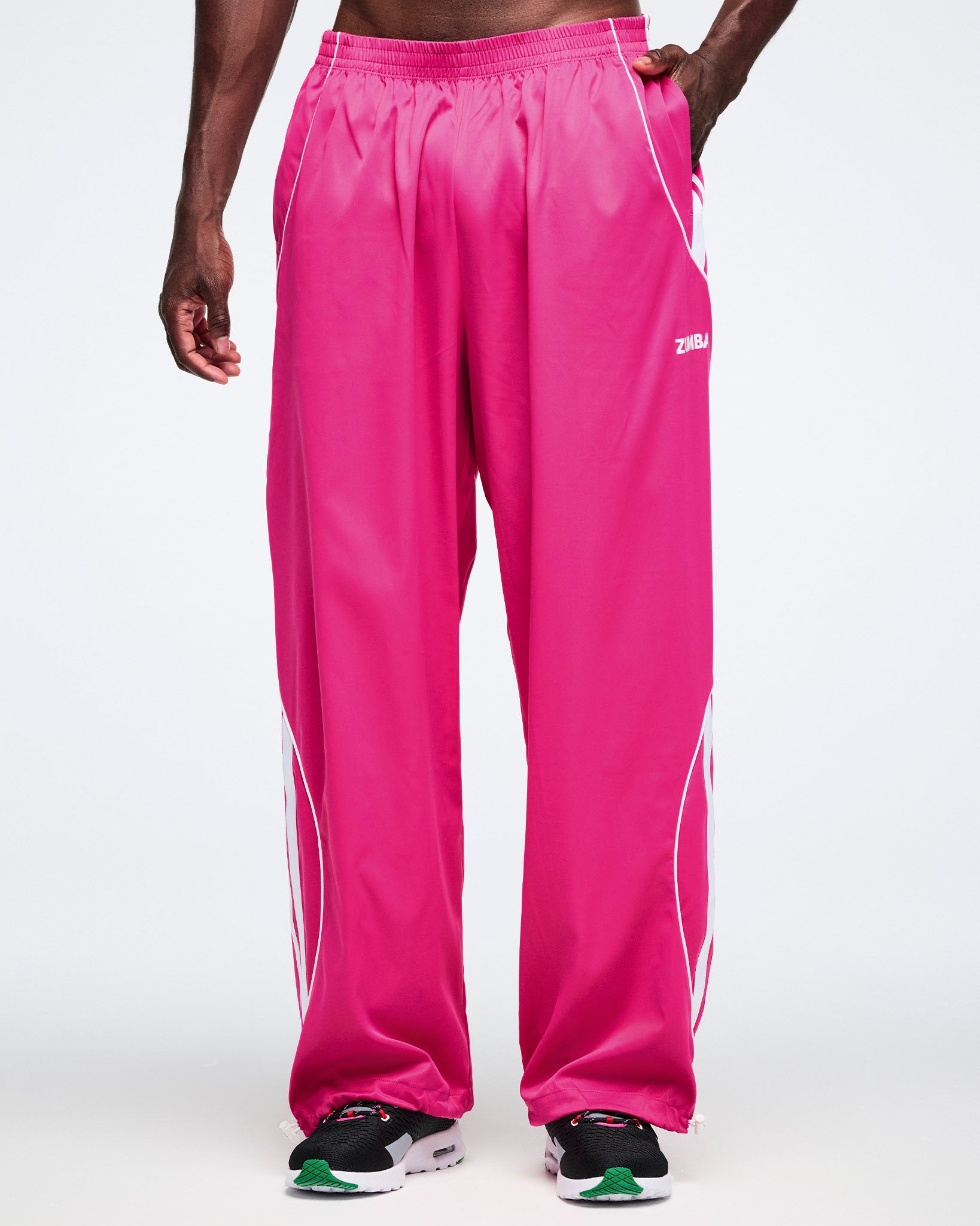 Male model wearing bright pink track pants with a Zumba logo on a white background.