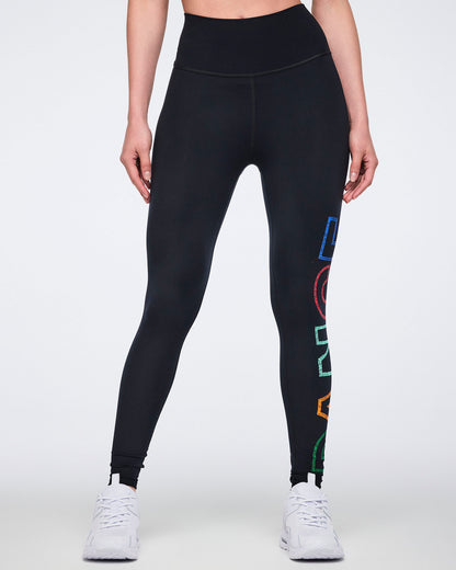Front view of black high-waisted full-length leggings with a sleek fitted shape and multicolor vertical “DANCE” graphic on one leg; half visible. Female model wears the leggings with white athletic sneakers.