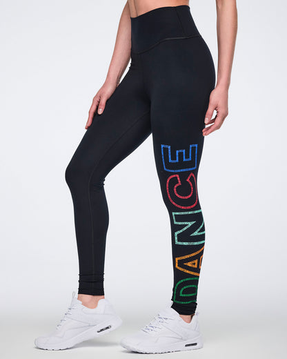 Side view of black high-waisted full-length leggings with a fitted silhouette and multicolor vertical “DANCE” graphic on one leg. Female model wears the leggings with white athletic sneakers.