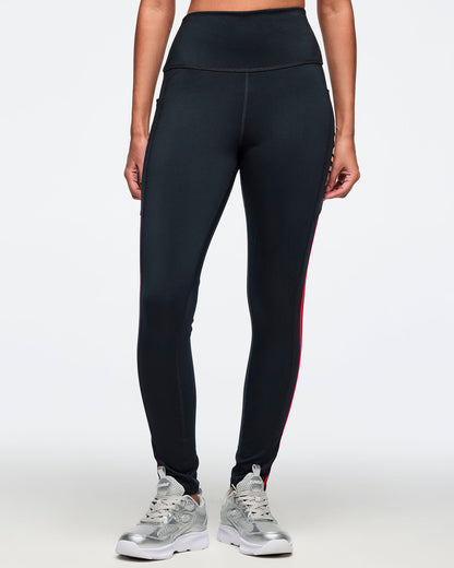 Black high-waisted leggings with a smooth fitted silhouette, side pockets, and bright coral pink side stripe details. Female model is wearing the full-length leggings with silver athletic sneakers.
