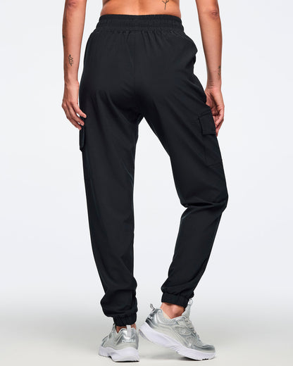 Black jogger pants shown from the back with an elastic waistband, cargo pockets, and tapered cuffed ankles. Female model is wearing the relaxed-fit joggers with silver athletic sneakers.