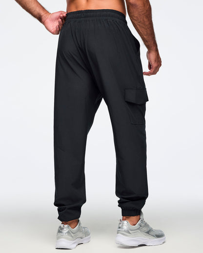 Black jogger pants shown from the back with an elastic waistband, cargo pockets, and tapered cuffed ankles. Male model is wearing the relaxed-fit joggers with silver athletic sneakers.