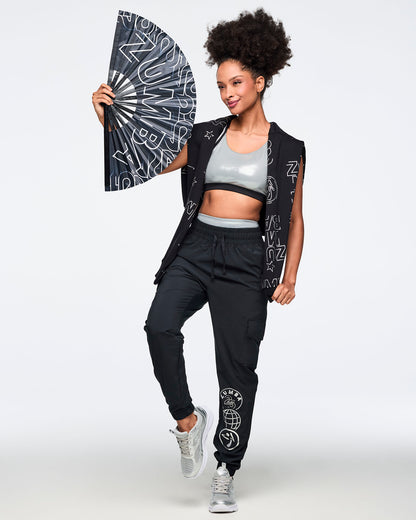 Black jogger pants with an elastic drawstring waistband, cargo pockets, and tapered cuffed ankles. Female model is wearing the relaxed-fit joggers with a silver sports bra, a black sweatshirt wrapped around her shoulders, and silver athletic sneakers.