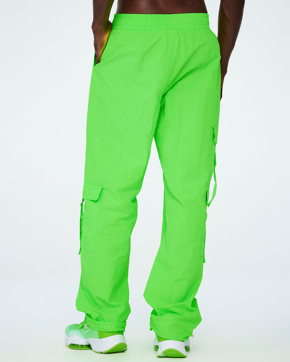 Shown from the back, a male model in the neon green tassel cargo pants, the wide straight legs falling over neon green shoes.