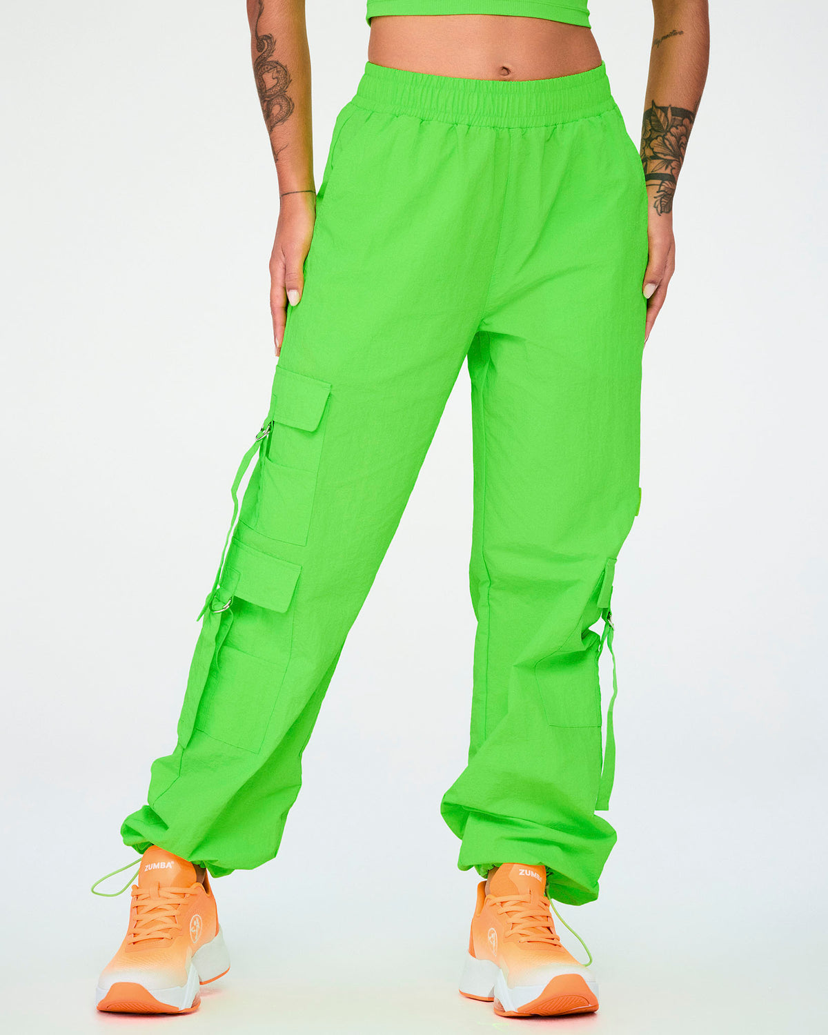 Female model in the neon green cargo pants with tassels, the hems drawn in with cords above orange shoes.