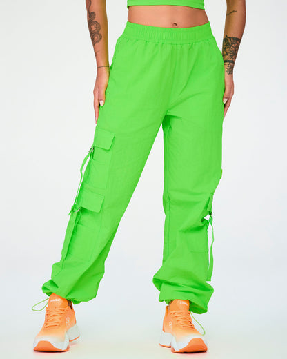 Female model in the neon green cargo pants with tassels, the hems drawn in with cords above orange shoes.