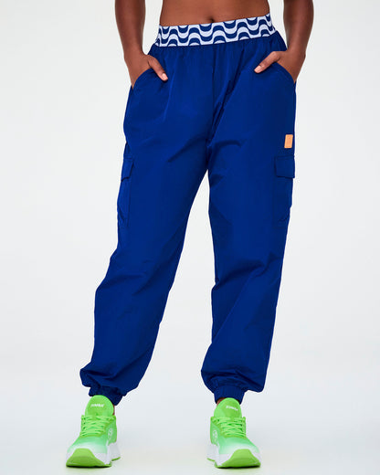 Female model in the blue parachute cargo pants, showing the roomy oversized leg, side cargo pockets, and the blue and white wavy waistband.