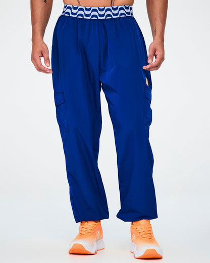 Male model in the blue parachute cargo pants with the orange tab, turned slightly to show the side cargo pocket and gathered cuffs above orange shoes.