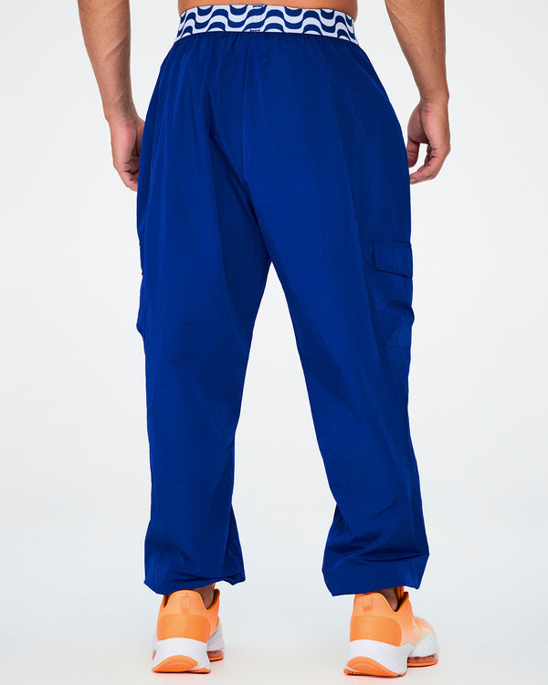 Back view of a male model in the blue parachute cargo pants, showing the blue and white wavy waistband and side cargo pockets.