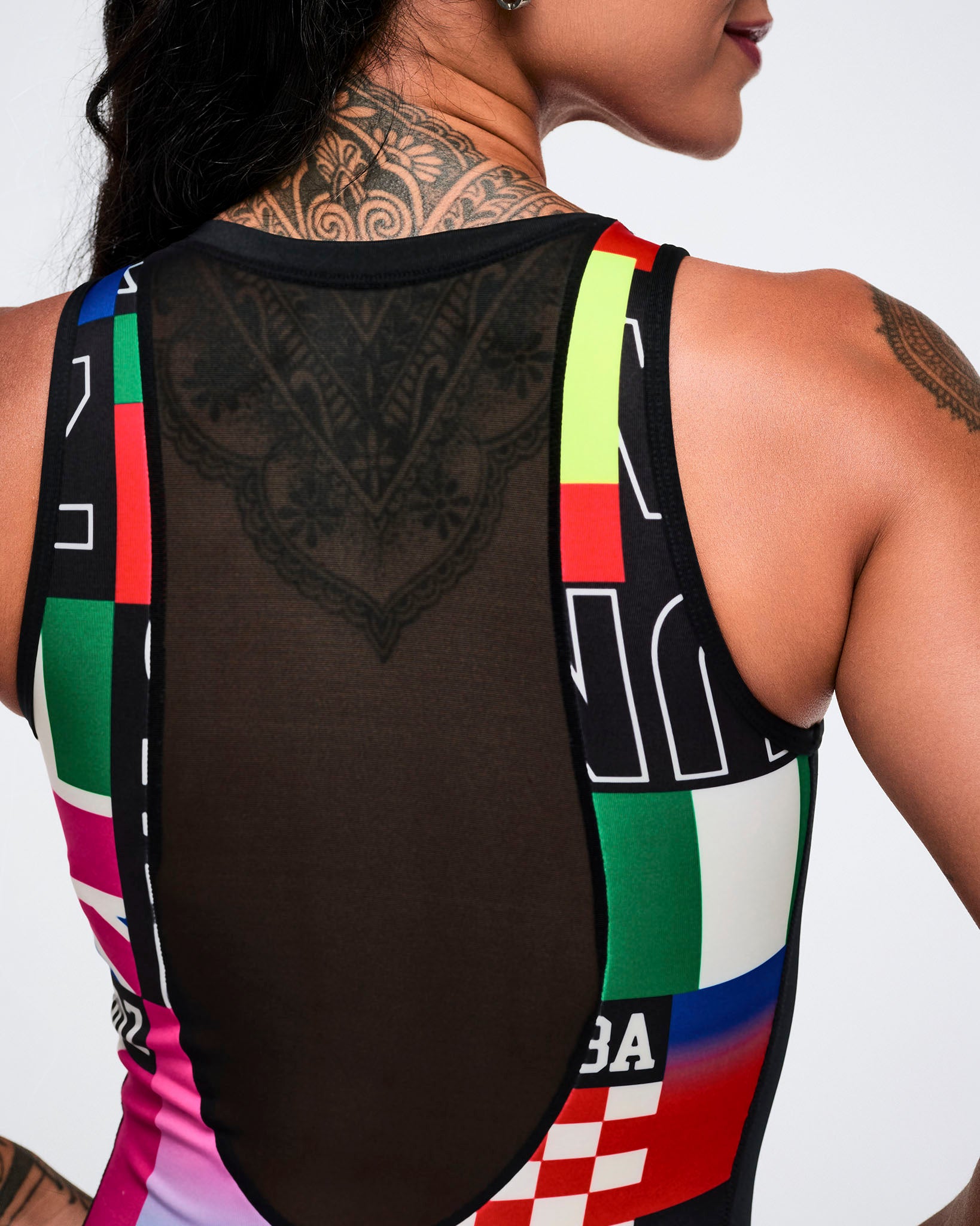 Close-up back view of a female model wearing a multicolored patterned bodysuit with an upper see-through black mesh.