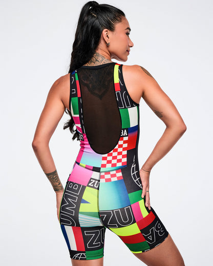 Back view of a female model wearing a multicolored patterned outfit with an upper see-through black mesh back against a white background.
