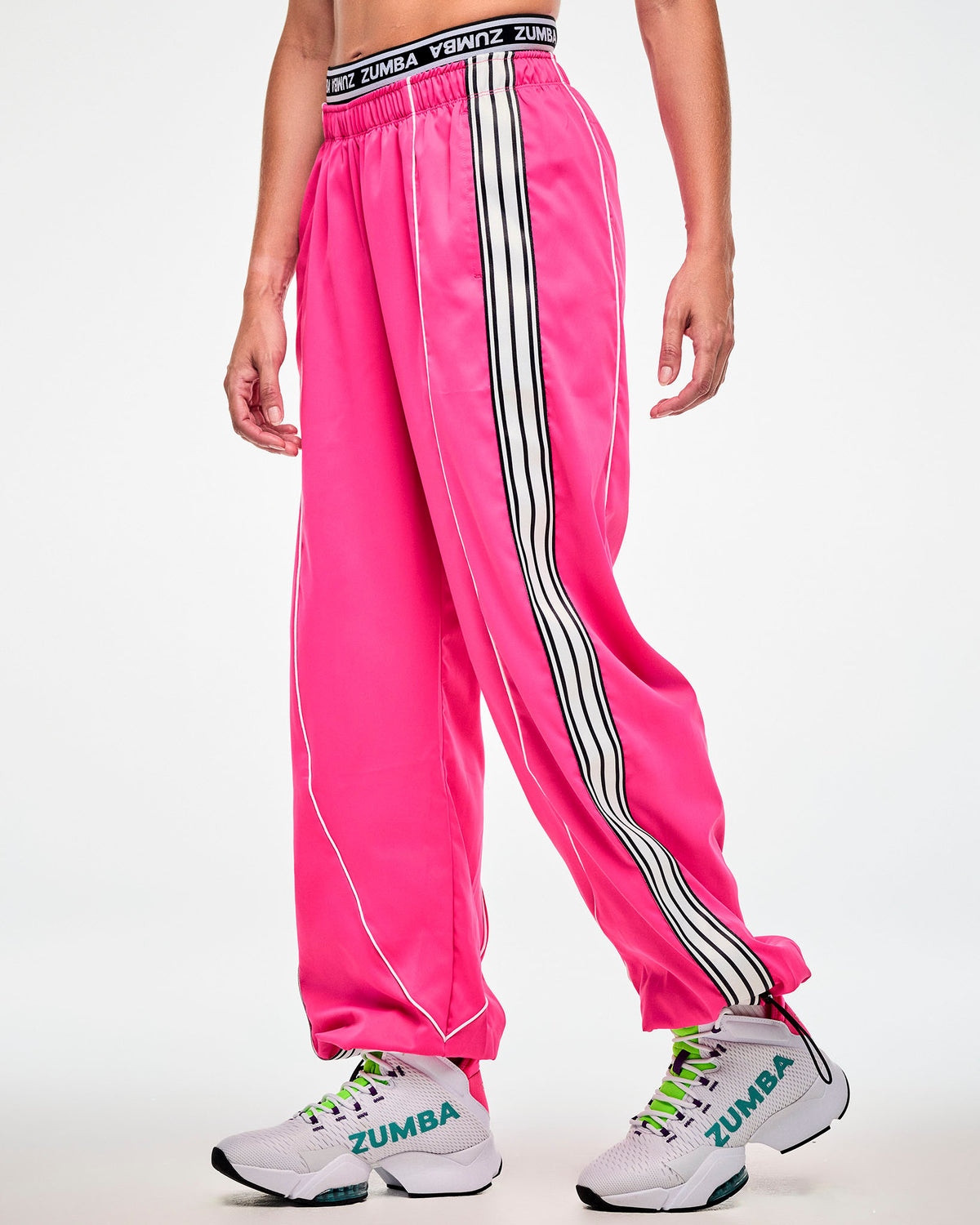 Female model wearing pink track pants with a white and black side stripe and white sneakers, side view.