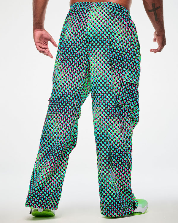 Shown from the back, male model wearing green cargo pants with an aqua, black, and pink dot print and green sneakers.